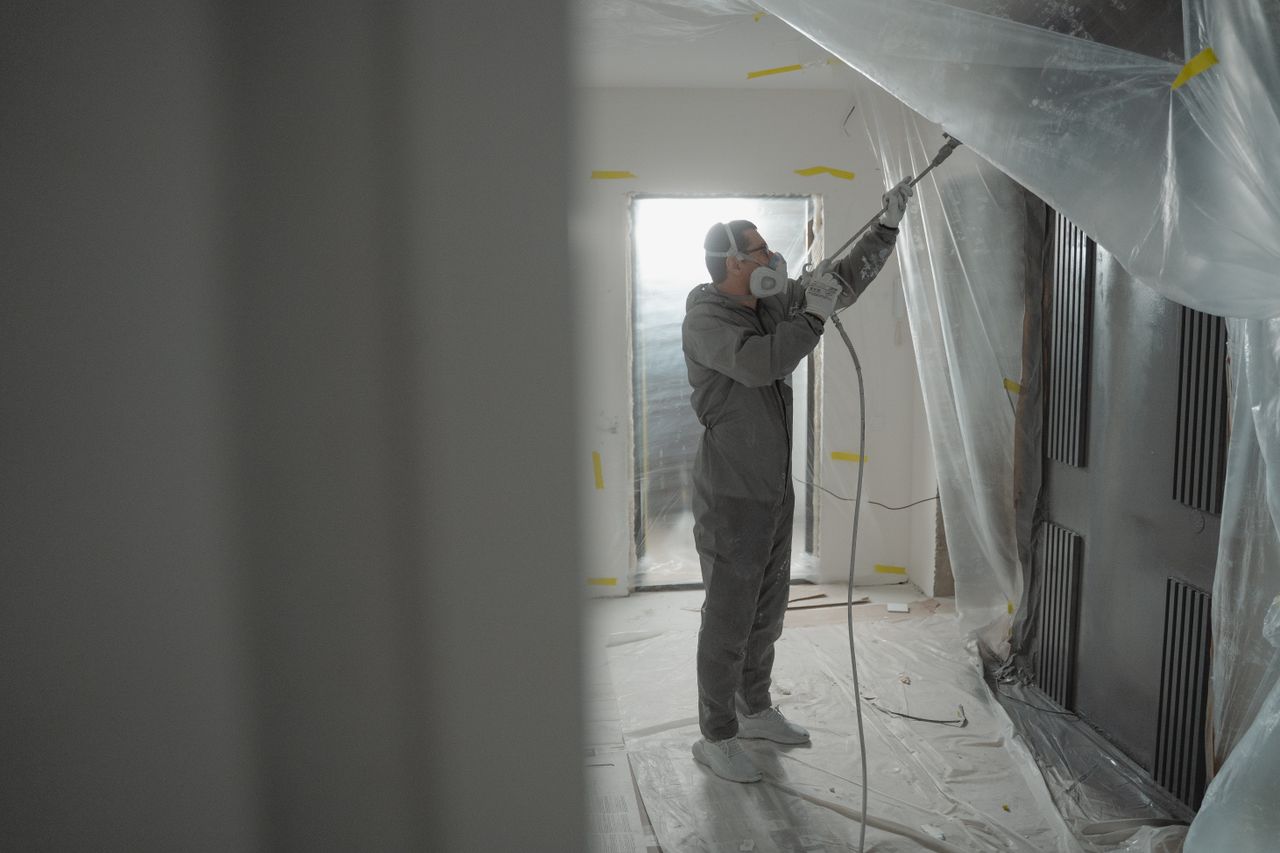 The Art of Drawing Readers In: Your attractive post title goes here Man in protective gear spray painting a house's interior during renovation work.