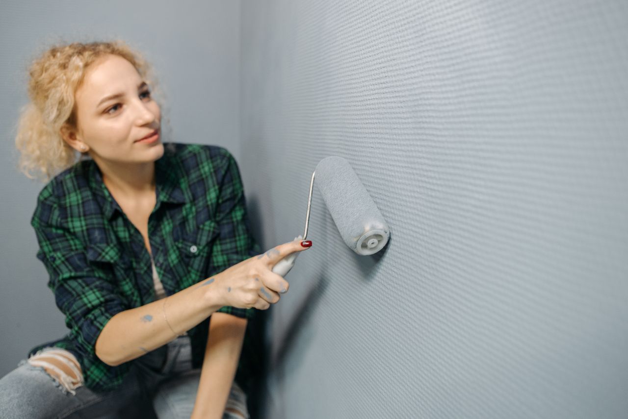 about-us A woman uses a paint roller to apply paint on a wall, part of a home renovation project.