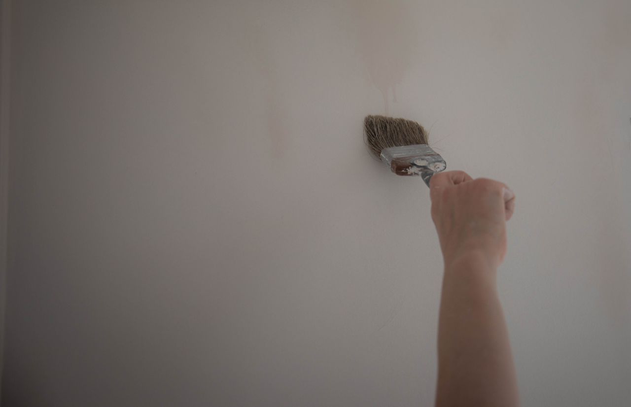 services-04 Hand using a paint brush to apply a coat of paint on a wall, highlighting DIY home improvement.