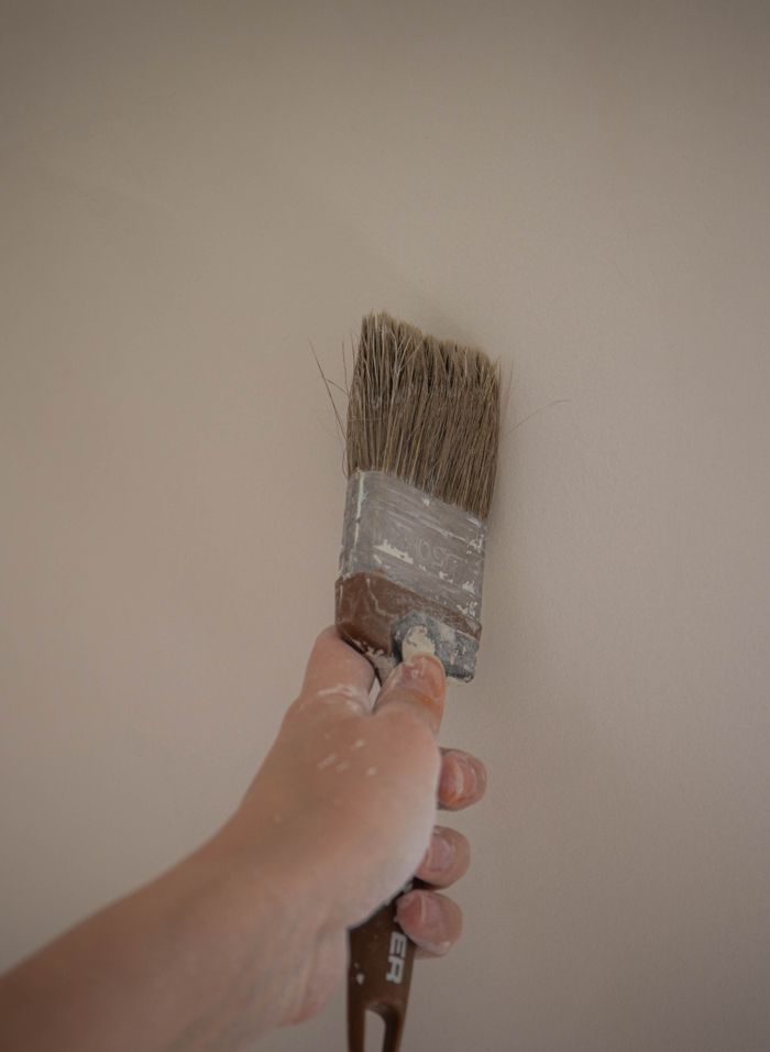 services-01 A hand painting an interior wall with a large brush, emphasizing DIY home improvement.